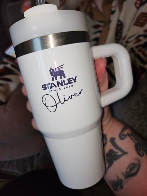 Person holding a white Stanley insulated tumbler with Oliver name personalization and black band, featuring the Stanley logo