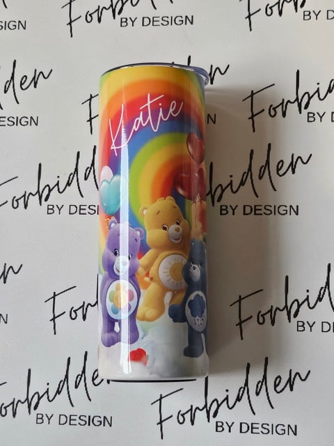 Personalized tumbler with rainbow gradient, Care Bears design, and name Katie printed on white surface with Forbidden By Design watermark